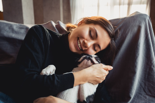 Um Boston Terrier e uma mulher abraçados em um sofá.