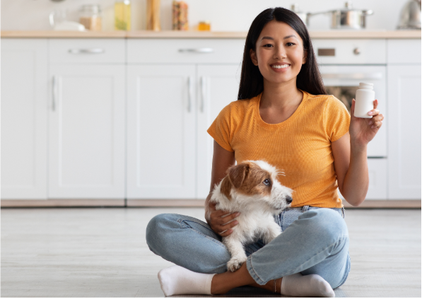 Uma mulher segurando um cão no colo, com um pote de suplementos na mão. 