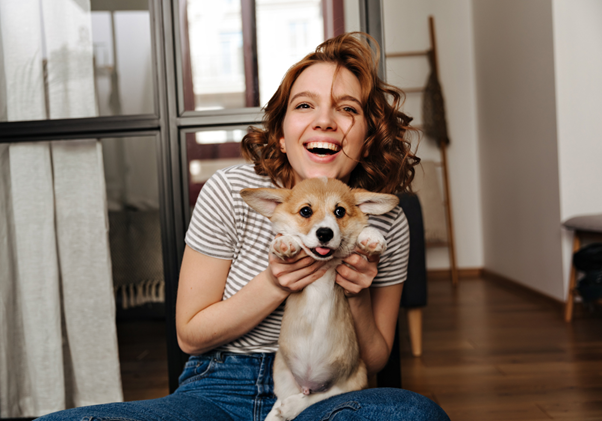 Uma mulher jovem segurando um cachorro enquanto sorri.